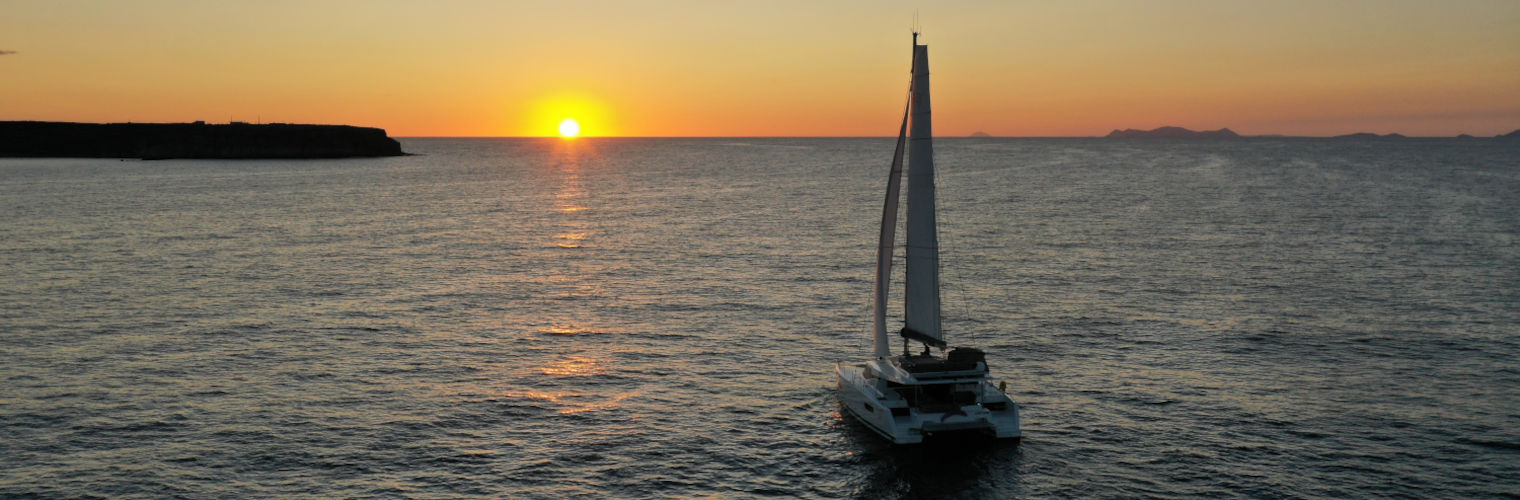 A catamaran in the sea with Santorini's sunset on the background