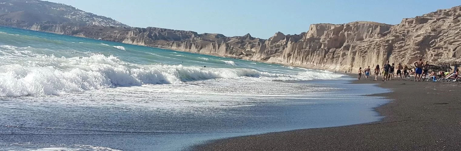 Waves crushing on a Santorini beach with white volcanic cliffs