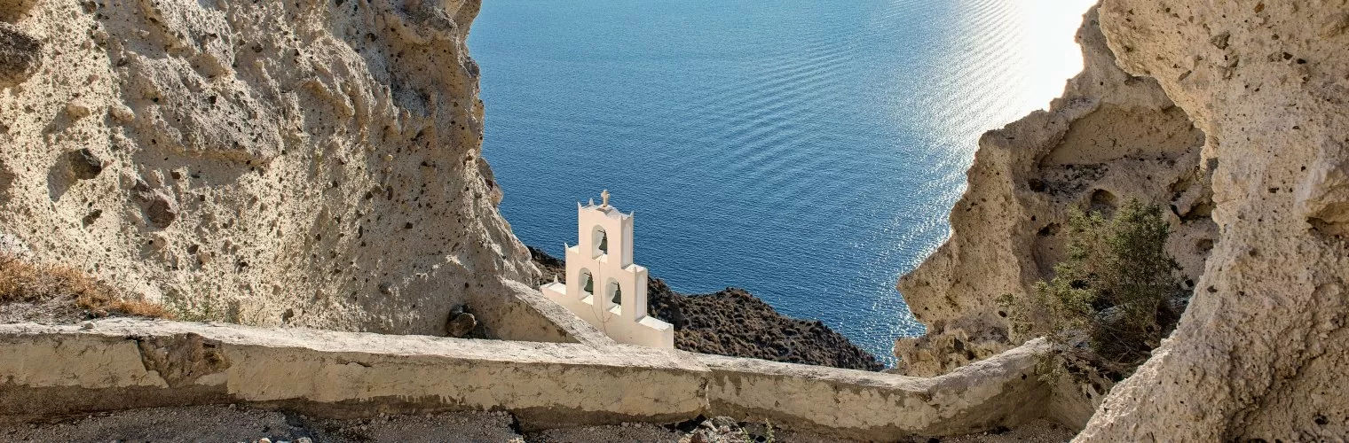 Volcanic cliffs with a white church and the Aegean sea on the background