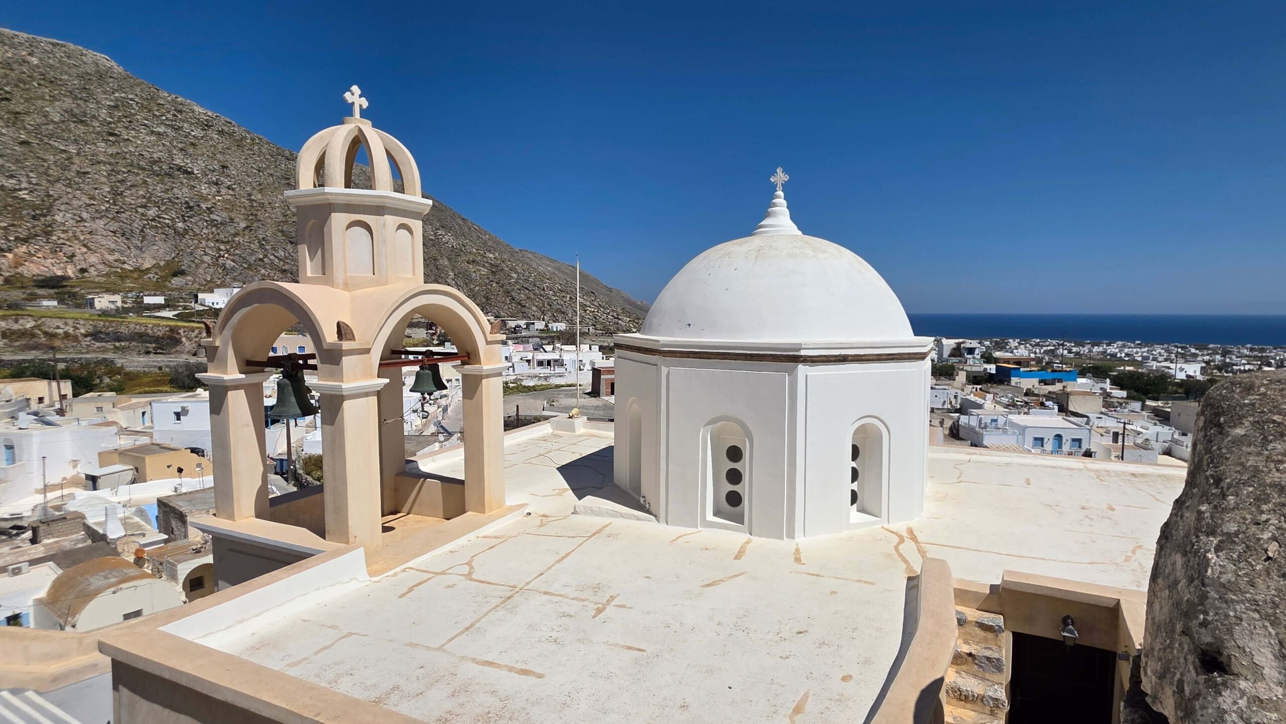 A church's rooftop featuring a bell tower and a white dome in Emporio, Santorini
