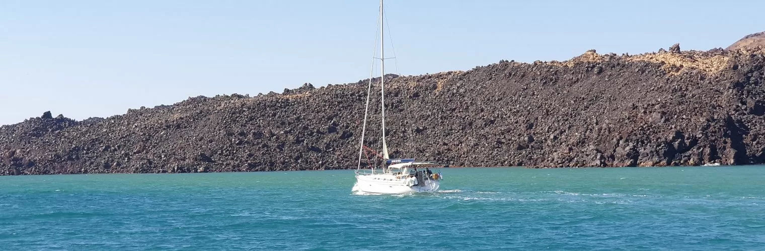 A yacht in blue-green Santorini waters with volcanic cliffs in the background