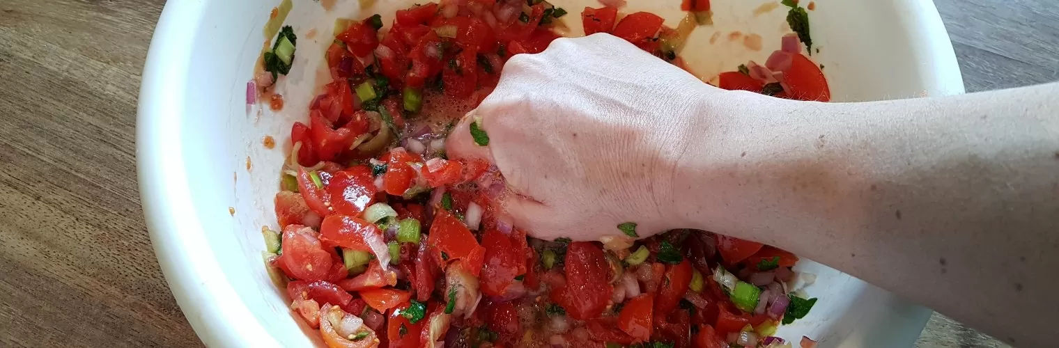 A hand mixing fresh chopped vegetables in a bowl during a Santorini online cooking class
