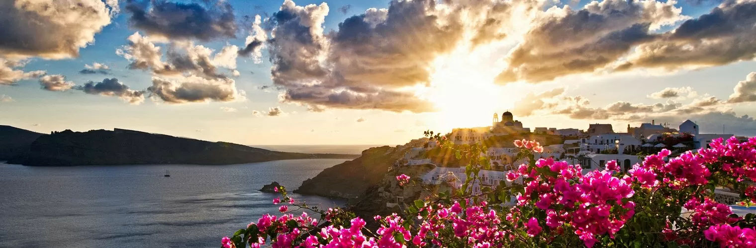 Sun setting behind the a cliff with pink flowers and white-washed houses as taken in a Santorini photo tour