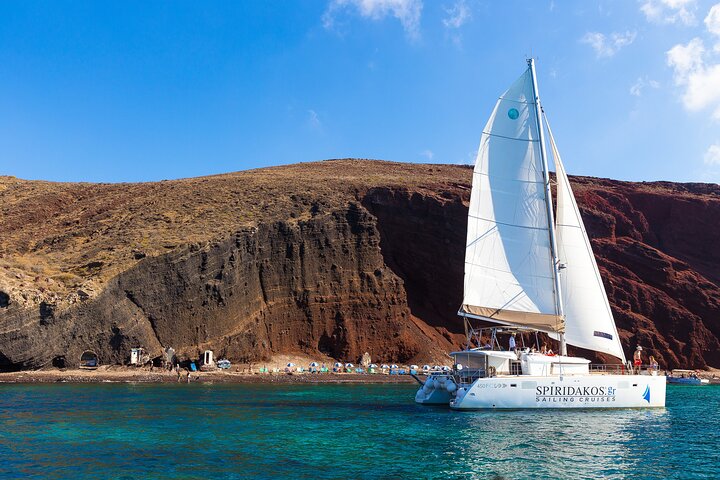 A catamaran sailing in turquoise water with volcanic cliffs on the background