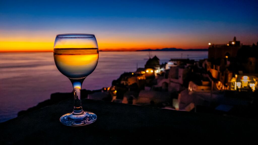 A white glass of wine with the sunset in the background during a Santorini wine tasting tour