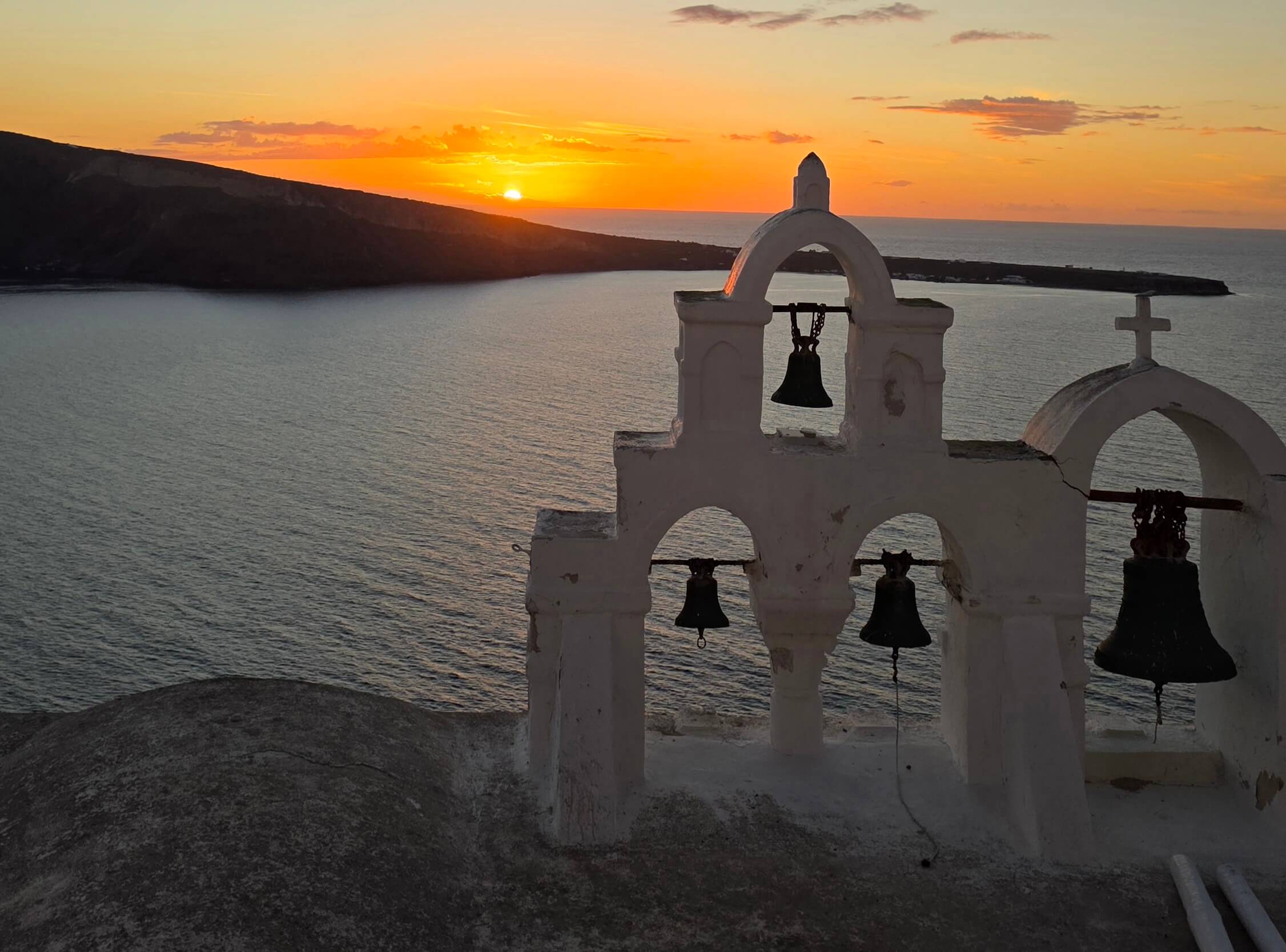 A church's 4-bell tower overlooking the Santorini sunset