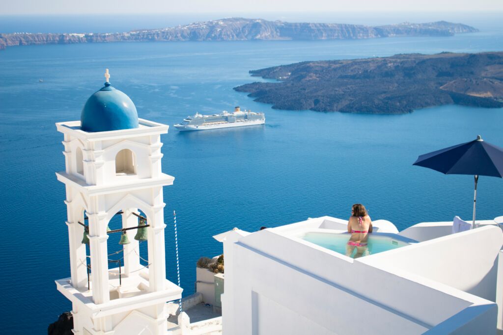 Woman in a roof pool overlooking a Santorini blue dome and the Aegean Sea